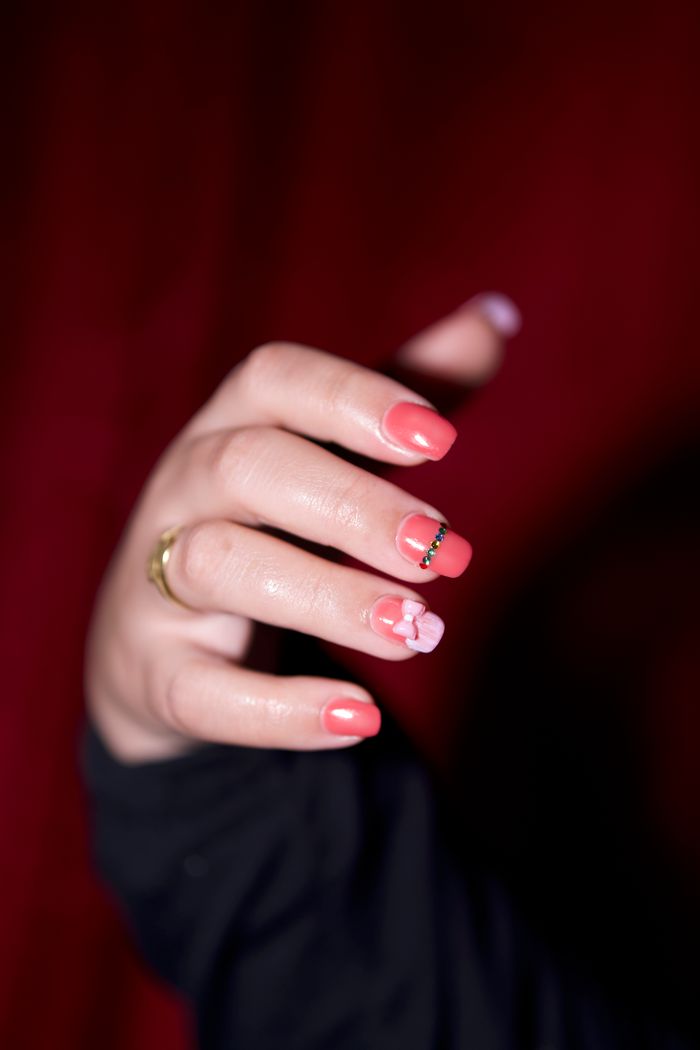 A detailed close-up of manicured nails with pink polish and floral accents, set against a dark background.